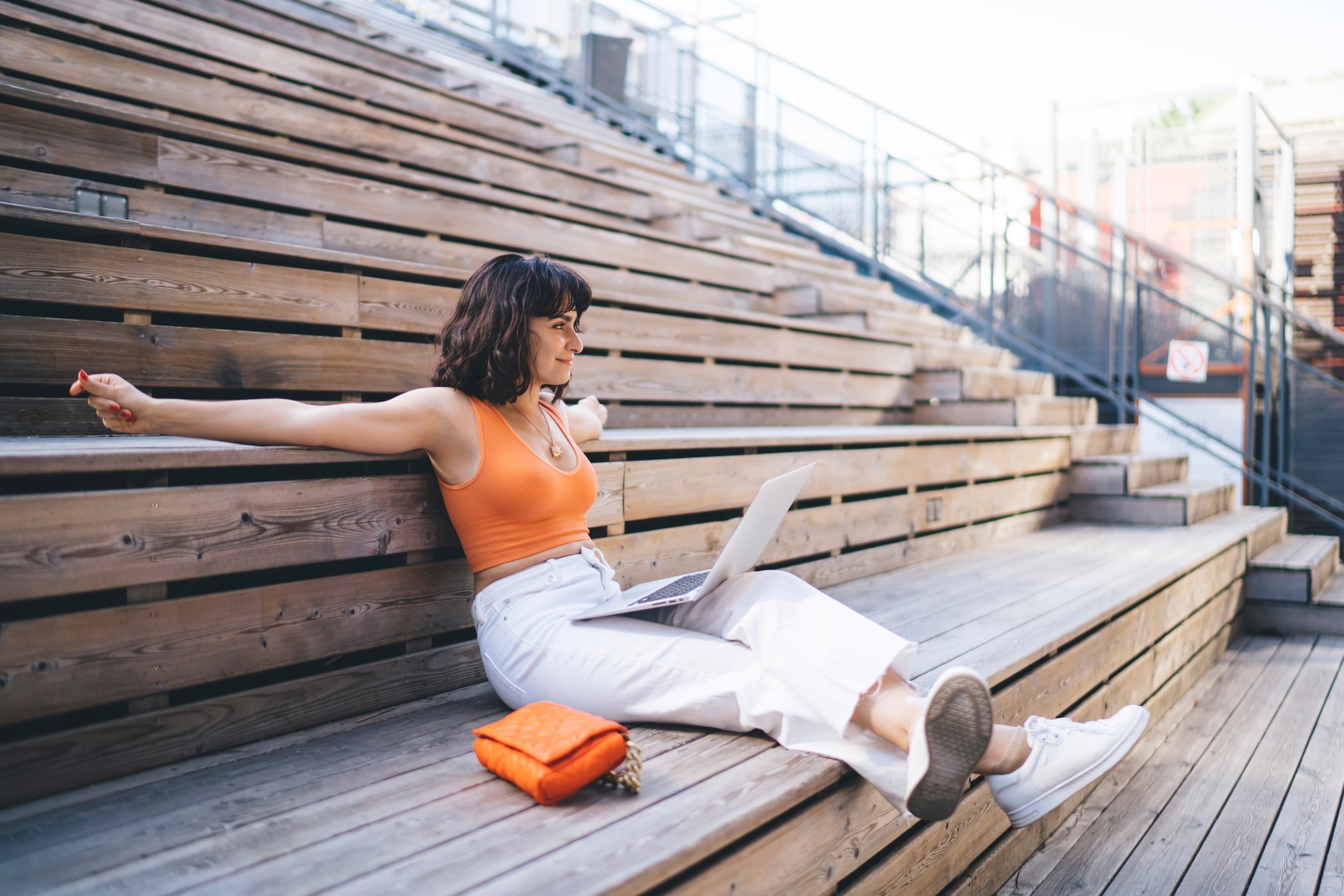 Positive woman watching webinar on laptop at wooden stairs